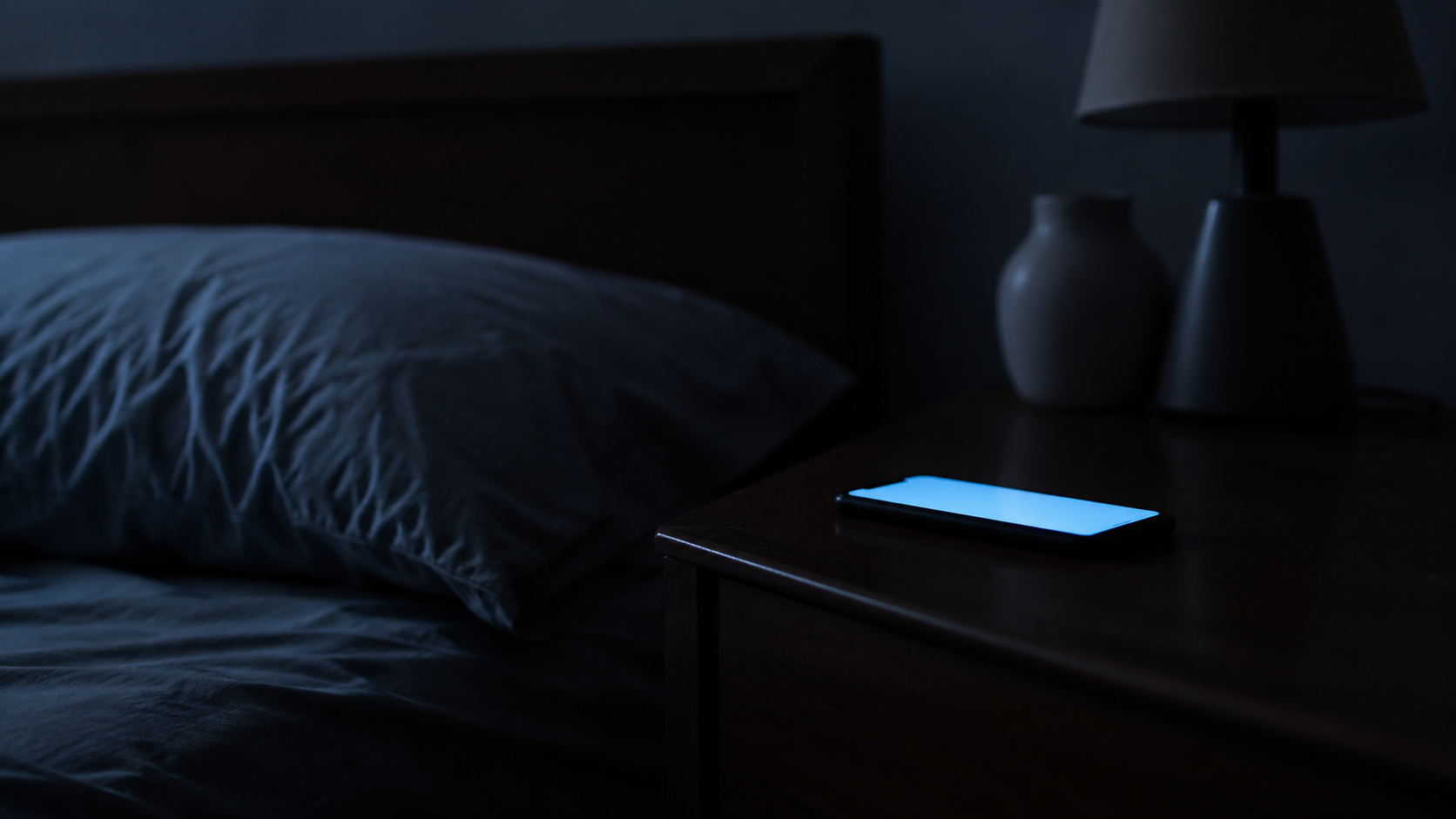 深夜の暗い寝室で、枕元のスマートフォンだけがぼんやり光っている様子