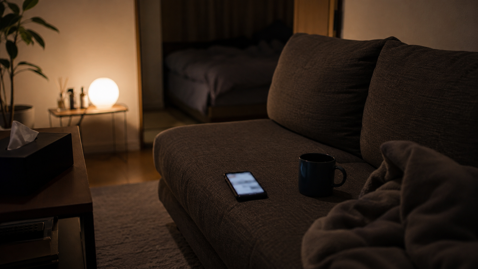 ソファに置かれたスマホとマグカップ、休んでも疲れが抜けない時間