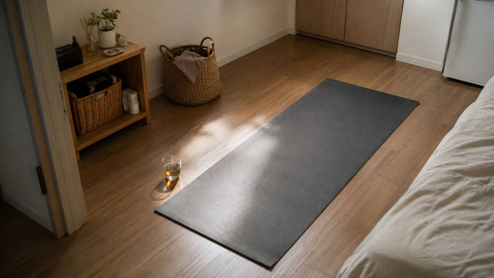 部屋の床にヨガマットが広げられているが、まだ誰も乗っていない。窓から日が差し、マットの横に飲み物の入ったコップが置かれている