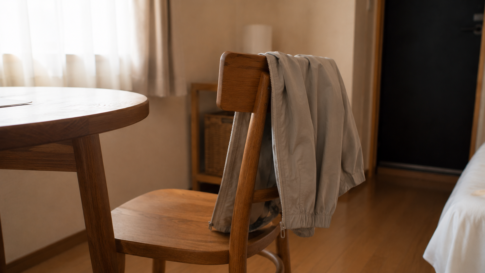 木の椅子の背もたれに、薄手のグレーのアウターが一枚かけられている部屋の様子