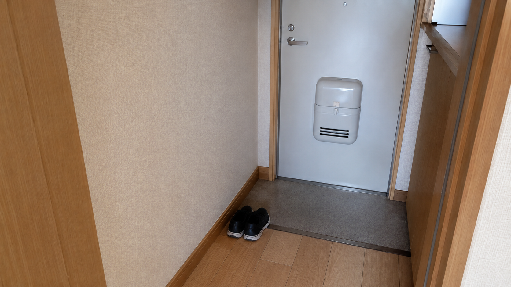 同じ玄関のそば。段ボールもゴミ袋もなく、床と壁に何も置かれていない。靴が一足だけそろえてある