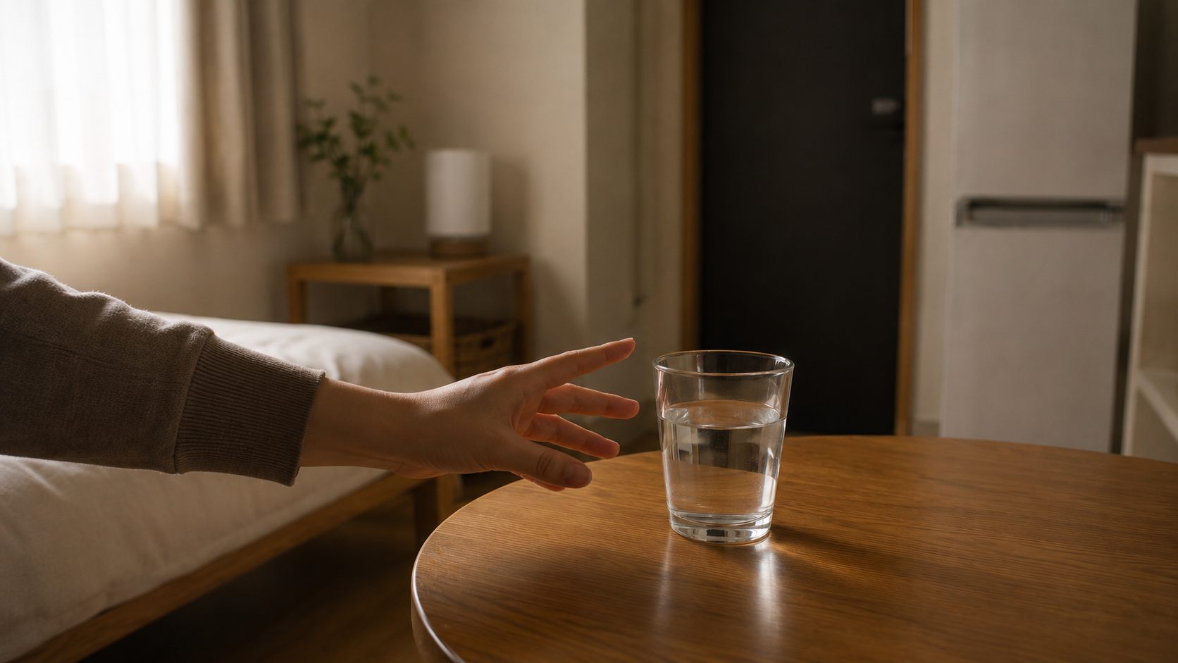 朝、静かな部屋でテーブルの上のコップの水へ伸ばす手
