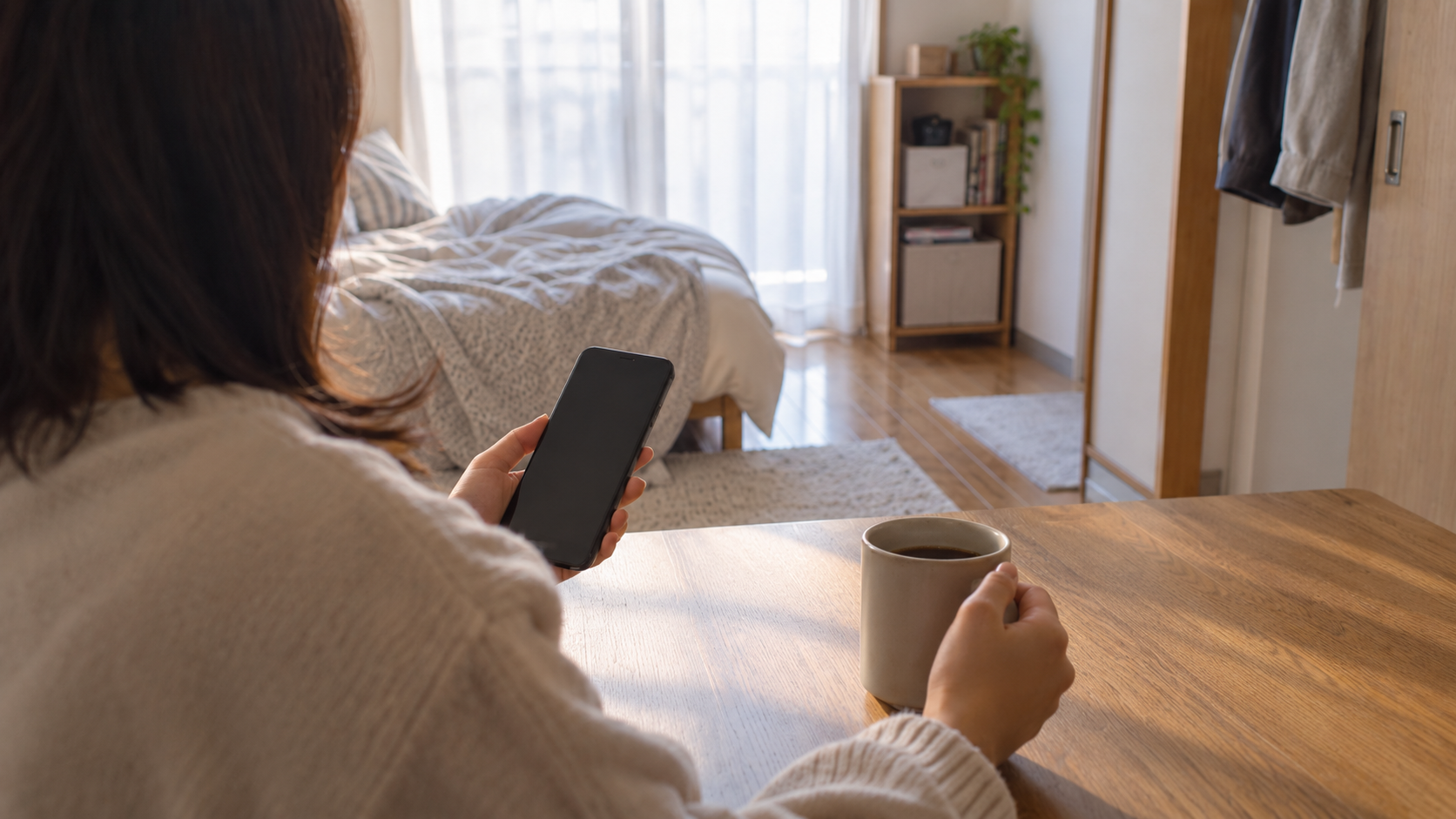 朝の窓辺でスマホとマグカップを持つ手元
